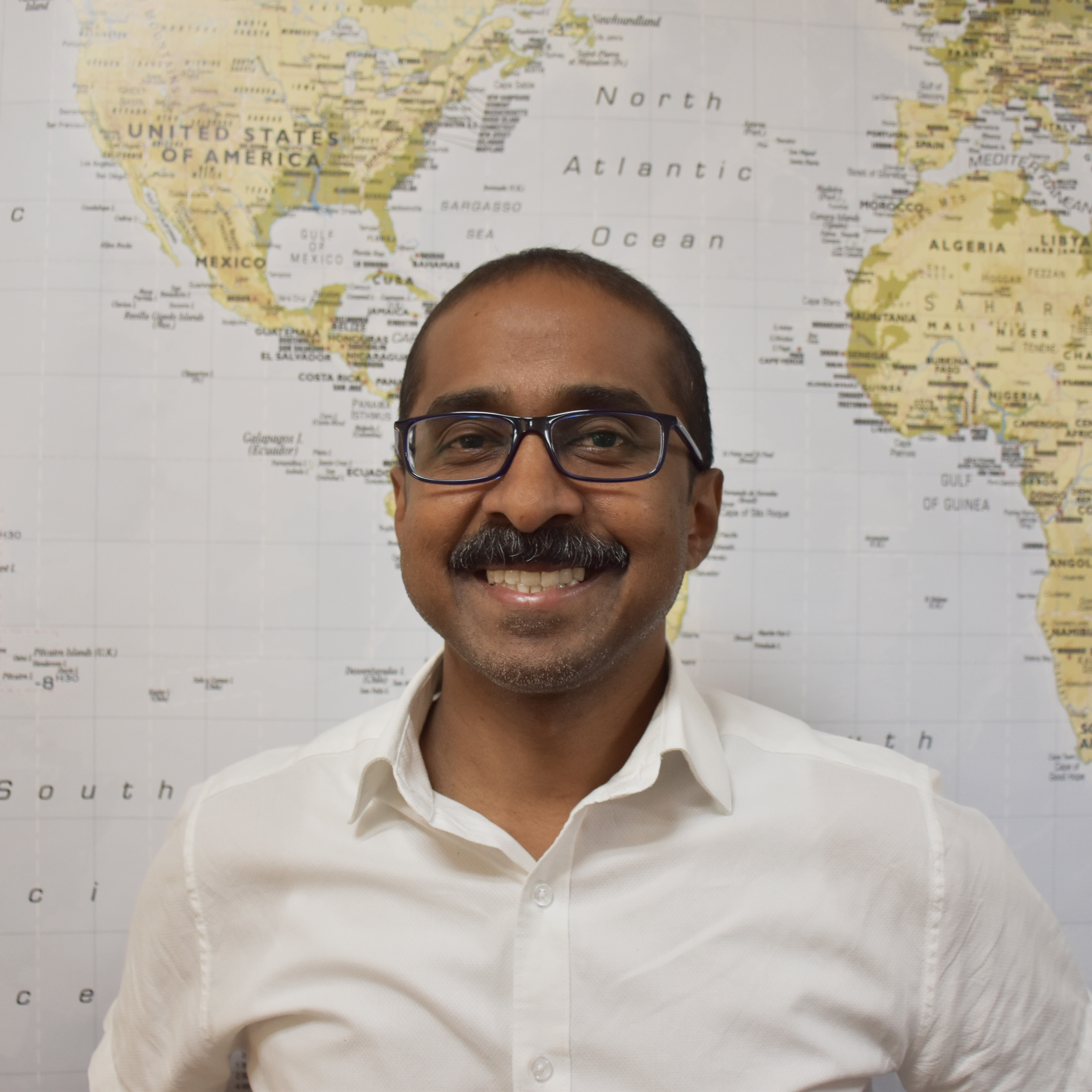 Jay Arasan, Associate Director smiling in front of world map